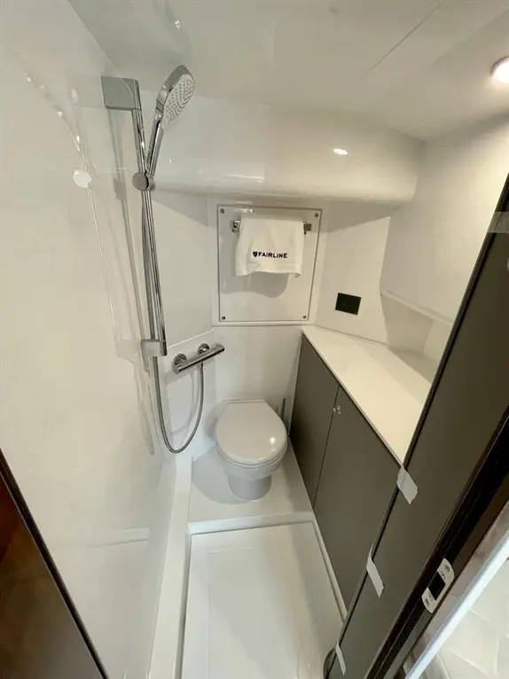 Compact bathroom with shower, toilet, and sleek cabinetry; features a towel labelled 'FAIRLINE'.